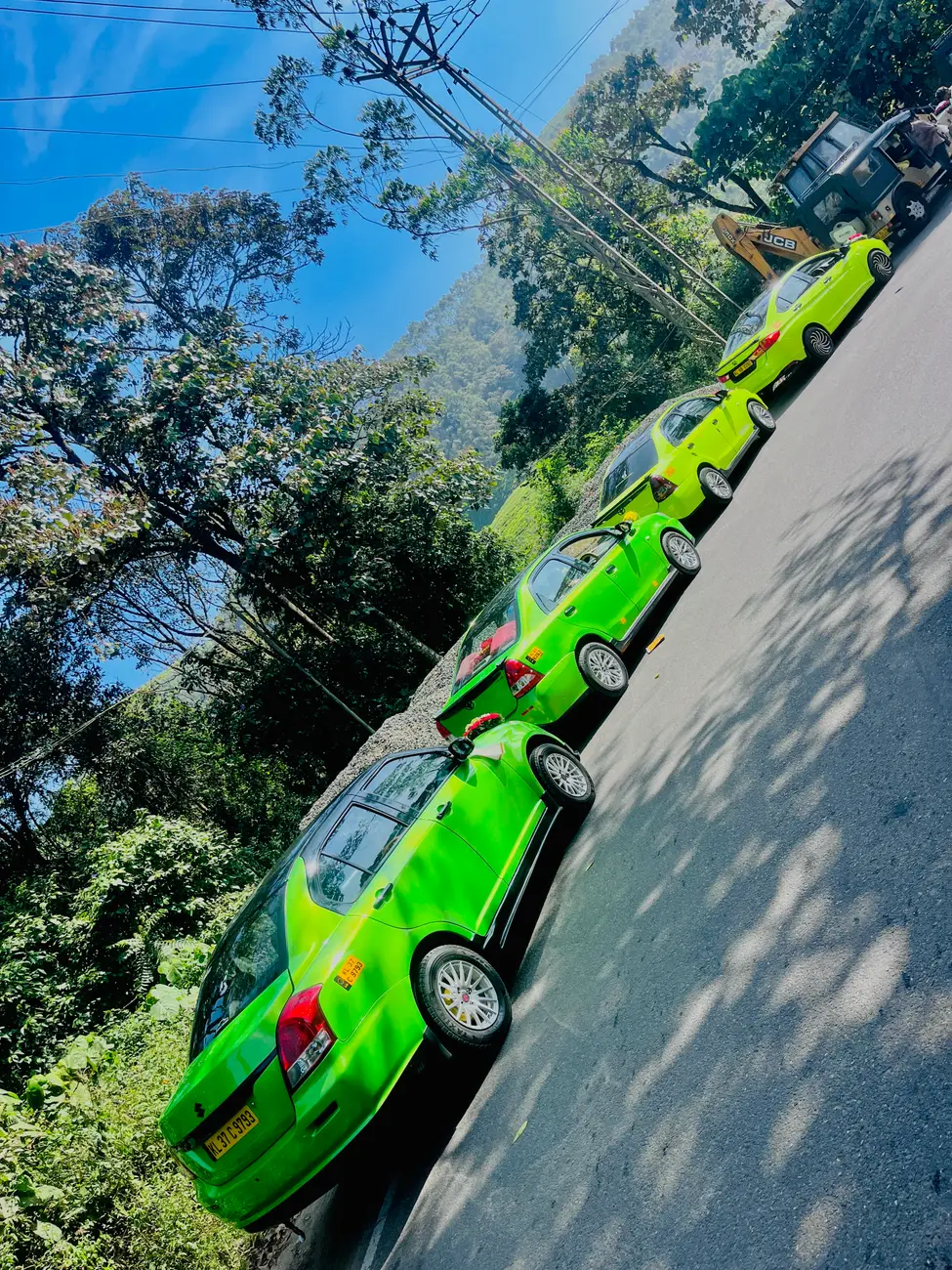 A convoy of green Munnar Trip Makers cabs parked along a hill road